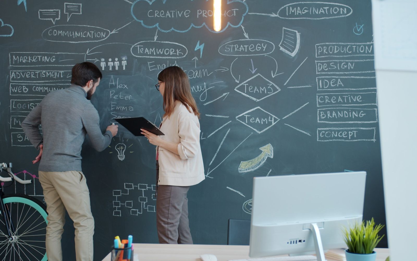 Dois colegas estrategizando sobre conceitos de negócios usando um quadro-negro em um escritório moderno