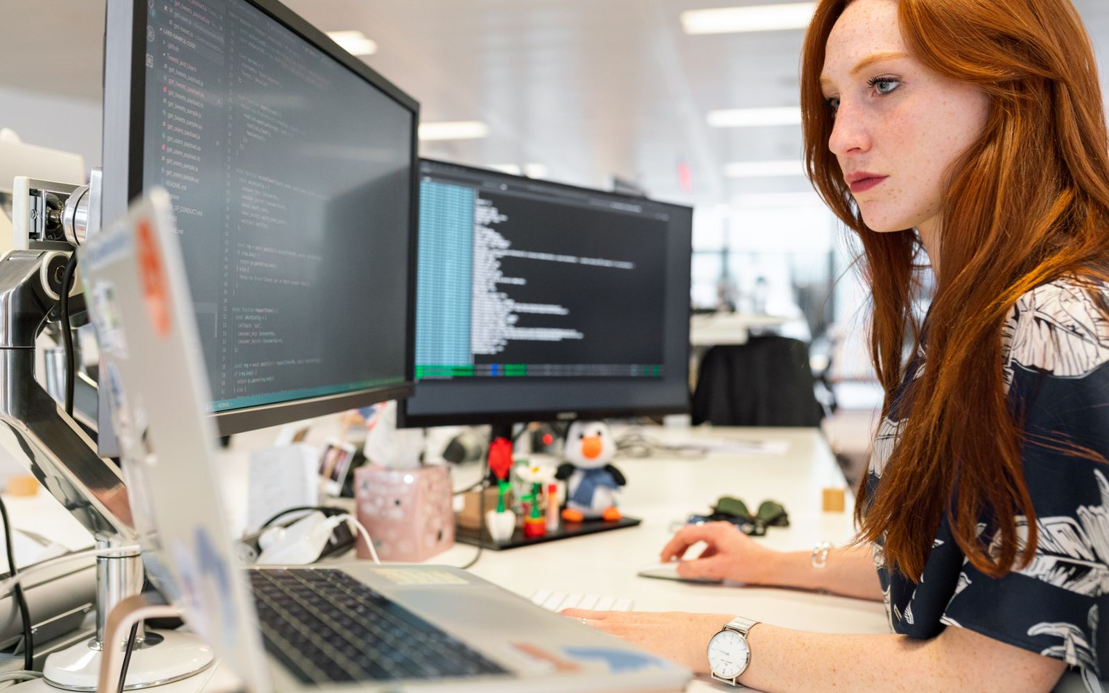 Uma engenheira de software feminina focada codificando em dois monitores em um escritório moderno