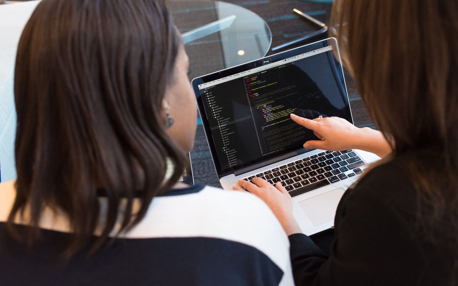 Duas mulheres trabalhando juntas em programação de software em ambiente interno, concentradas no código