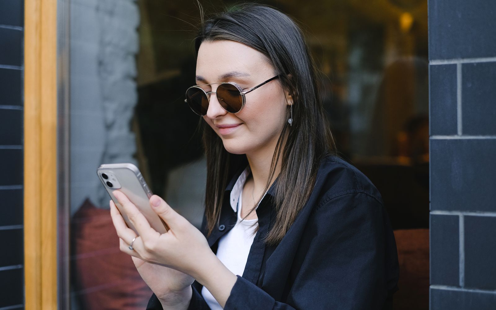 Uma jovem com óculos de sol sorri enquanto usa seu smartphone ao ar livre