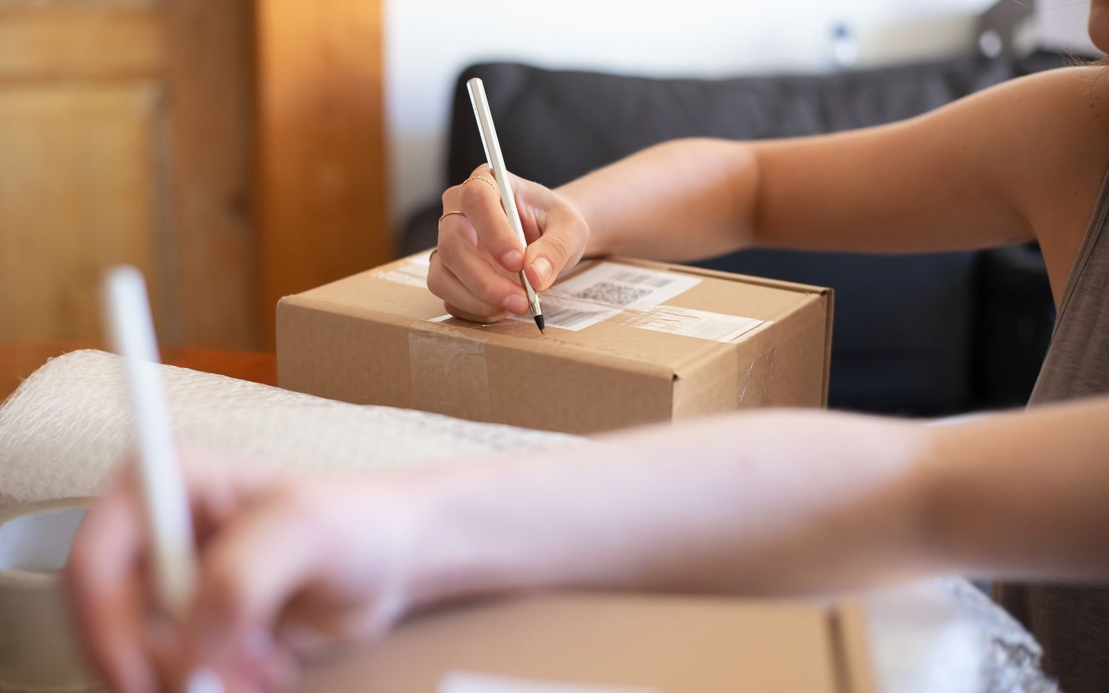 Mãos etiquetando uma caixa de papelão para envio, em escritório em casa