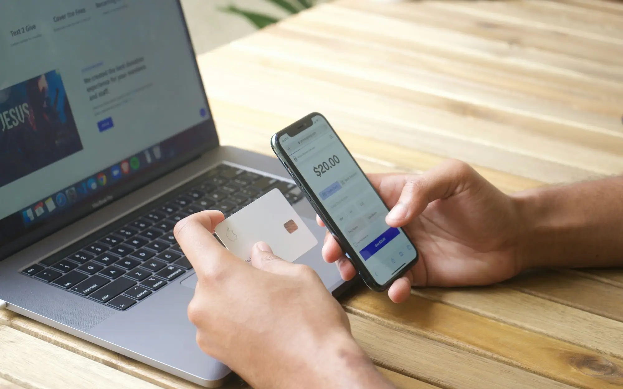 Compra pelo celular com o cartão na mão, ao lado do notebook
