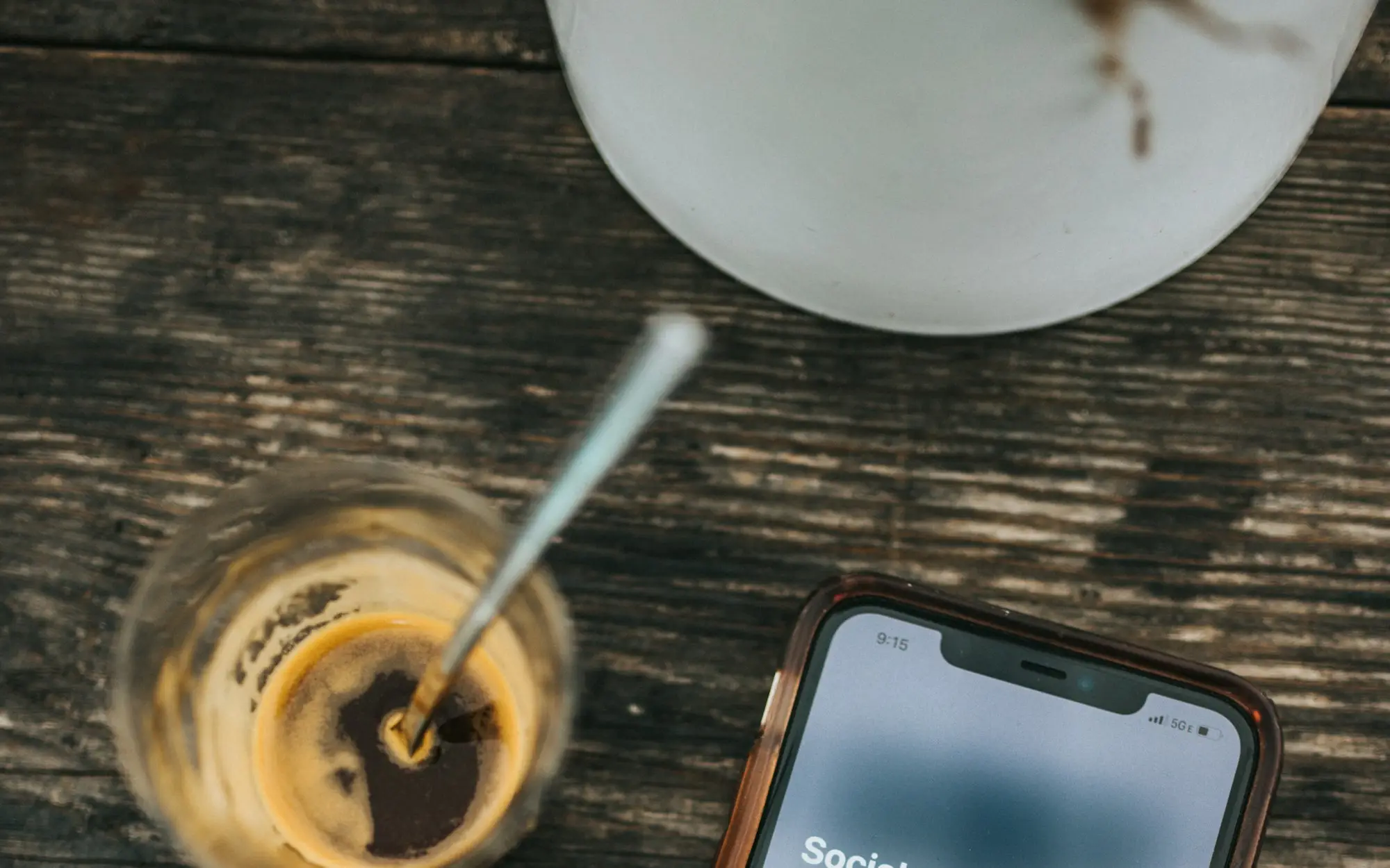 Celular sobre a mesa de madeira, ao lado de um café